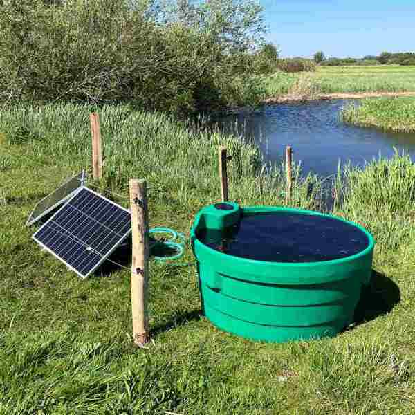 Soldriven markpump med solpanel och vattentråg vid en bäck på en äng.