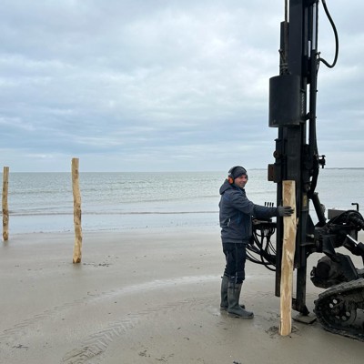 Montör sätter upp trästolpar med maskin på en strand vid kusten.